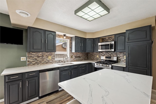 kitchen featuring light stone countertops, light wood-style flooring, stainless steel appliances, backsplash, and a sink