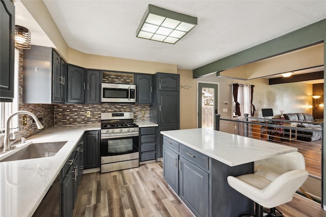 kitchen with a sink, appliances with stainless steel finishes, a kitchen island, wood finished floors, and backsplash