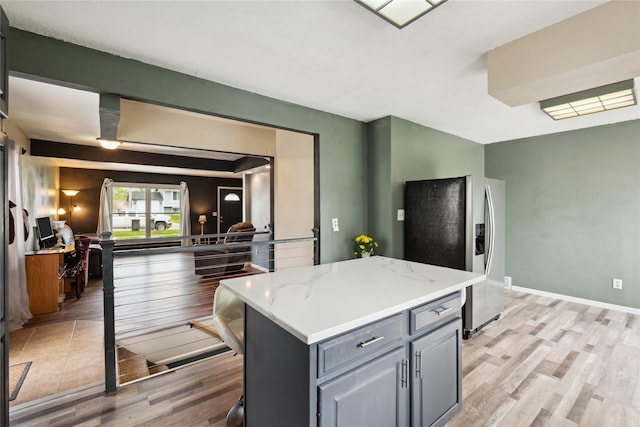 kitchen featuring light stone countertops, gray cabinets, light wood-type flooring, a kitchen island, and stainless steel fridge with ice dispenser