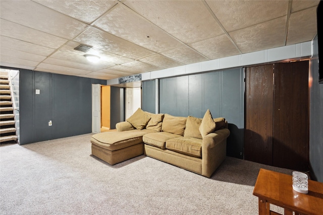 living area featuring visible vents, a decorative wall, carpet flooring, and stairs