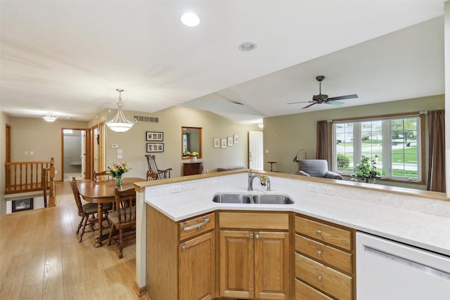 kitchen with a sink, light countertops, dishwasher, light wood finished floors, and decorative light fixtures