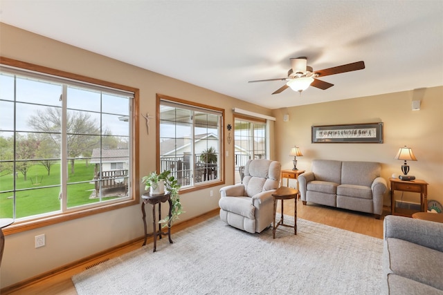 living room featuring wood finished floors, a ceiling fan, visible vents, and baseboards