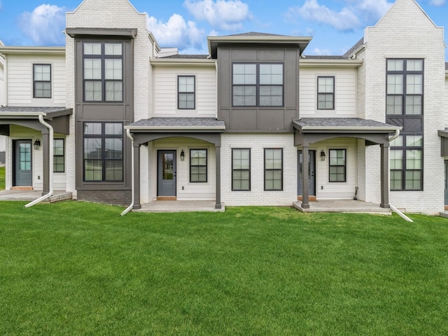 townhome / multi-family property featuring a front yard, a shingled roof, and brick siding