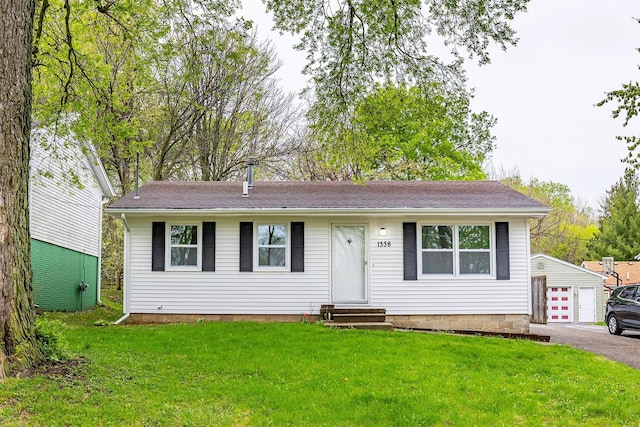 single story home featuring entry steps, a detached garage, a shingled roof, and a front lawn
