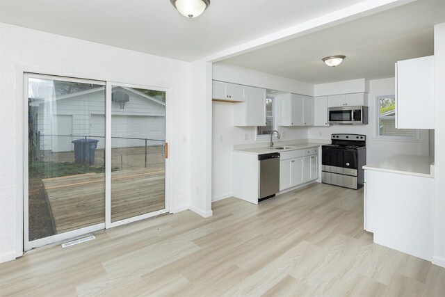 kitchen with light wood-style flooring, light countertops, a sink, stainless steel appliances, and white cabinetry