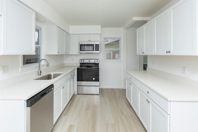kitchen with light countertops, white cabinetry, a sink, light wood finished floors, and appliances with stainless steel finishes