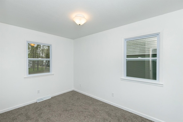 unfurnished room with baseboards, visible vents, and dark colored carpet