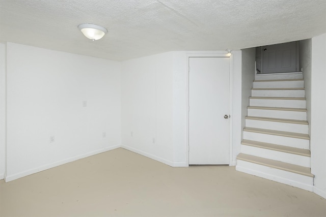 finished below grade area featuring baseboards, stairs, and a textured ceiling