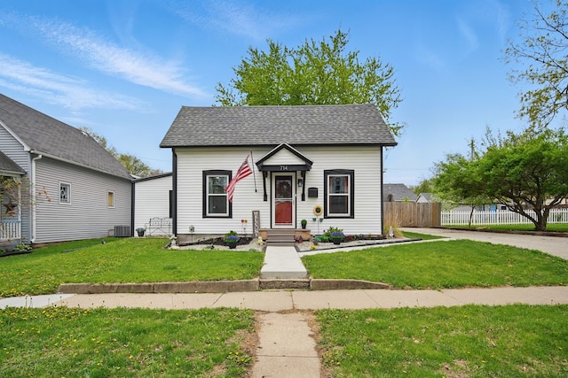view of front of house with a front yard, a shingled roof, and fence