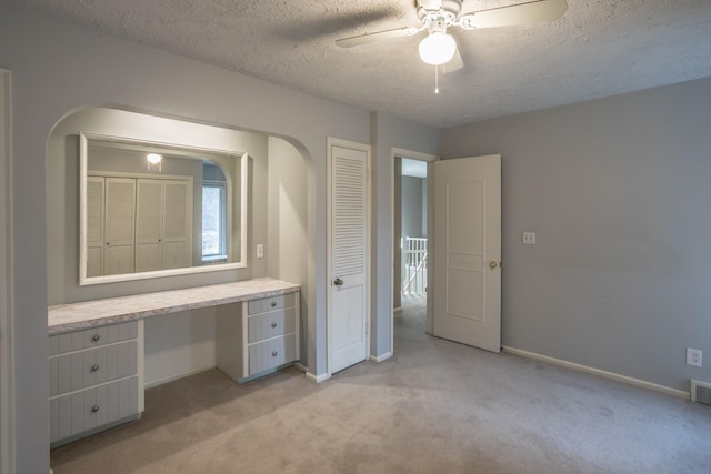 unfurnished bedroom featuring a textured ceiling, ceiling fan, baseboards, built in study area, and light carpet