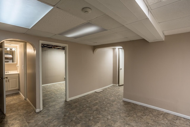 finished basement featuring baseboards, arched walkways, dark floors, and a paneled ceiling