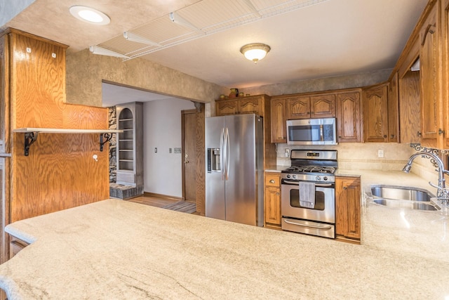 kitchen featuring a sink, appliances with stainless steel finishes, light countertops, a peninsula, and brown cabinetry