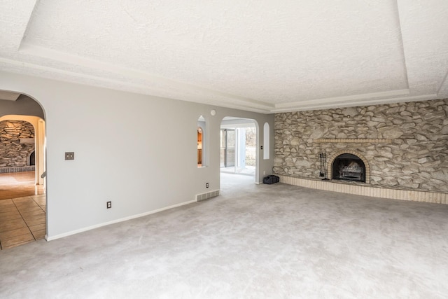 unfurnished living room featuring arched walkways, carpet flooring, a fireplace, visible vents, and a textured ceiling