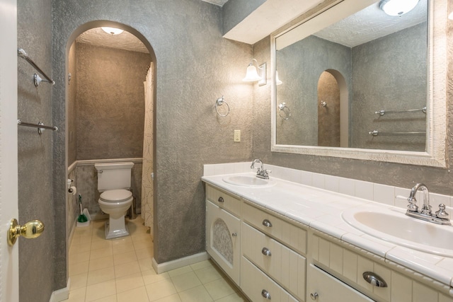 bathroom featuring tile patterned floors, toilet, double vanity, and a sink