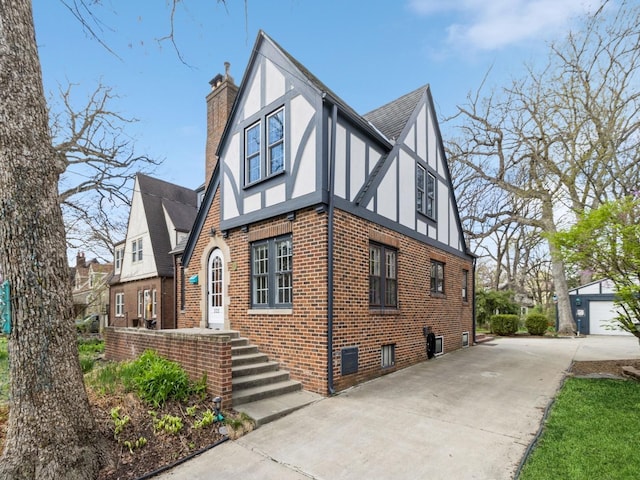 322 49th St, Des Moines, IA 50312 - view of side of home with concrete driveway, a chimney, brick siding, roof with shingles, and stucco siding