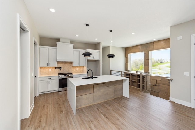kitchen with light wood finished floors, a sink, stainless steel range with gas stovetop, decorative backsplash, and light countertops