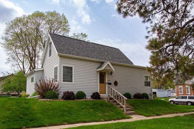 cape cod home featuring entry steps, a shingled roof, and a front yard