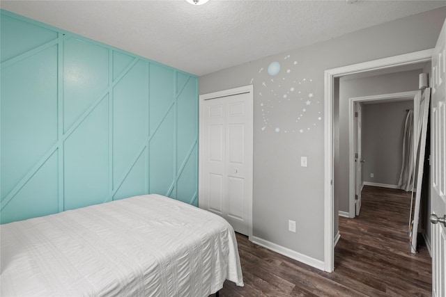 bedroom featuring dark wood-style flooring, a decorative wall, a textured ceiling, baseboards, and a closet