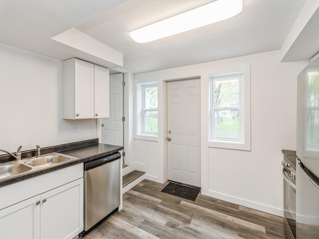 kitchen featuring dark countertops, a sink, dishwasher, white cabinetry, and wood finished floors