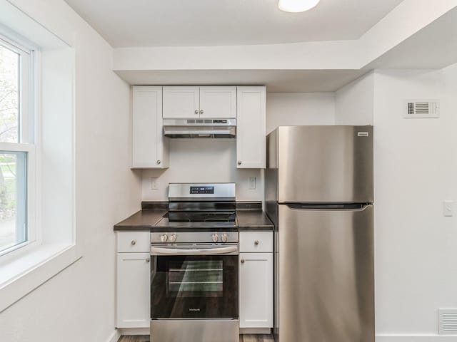 kitchen featuring visible vents, dark countertops, under cabinet range hood, white cabinets, and stainless steel appliances