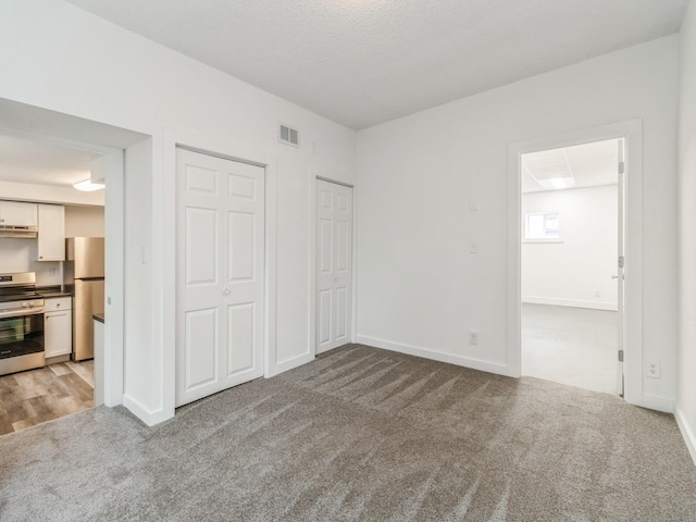 unfurnished bedroom featuring visible vents, freestanding refrigerator, multiple closets, light carpet, and connected bathroom