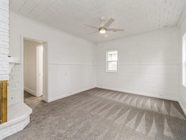 carpeted empty room with a fireplace with raised hearth, ornamental molding, a ceiling fan, and a wainscoted wall