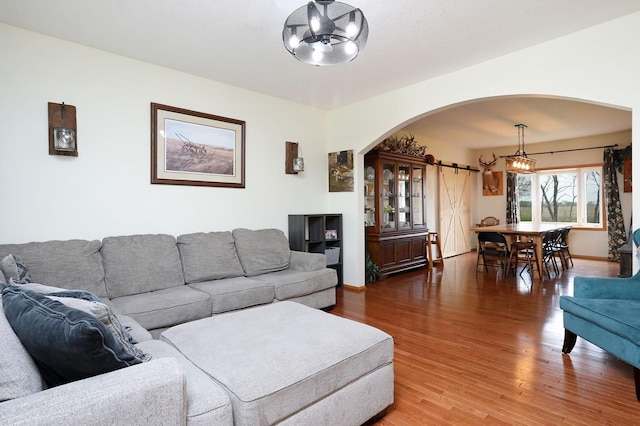living area featuring baseboards, arched walkways, wood finished floors, and a notable chandelier