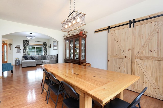 dining space featuring arched walkways, a barn door, and light wood-type flooring