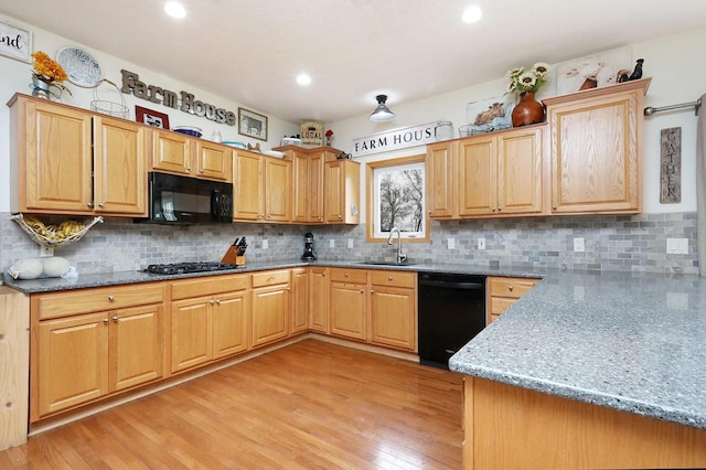 kitchen with decorative backsplash, light wood-type flooring, a sink, stone countertops, and black appliances
