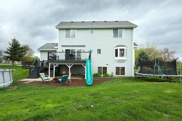 back of house featuring a trampoline, a yard, stairway, and a deck