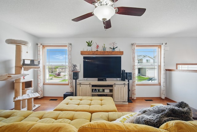 living area with baseboards, ceiling fan, light wood finished floors, and a textured ceiling