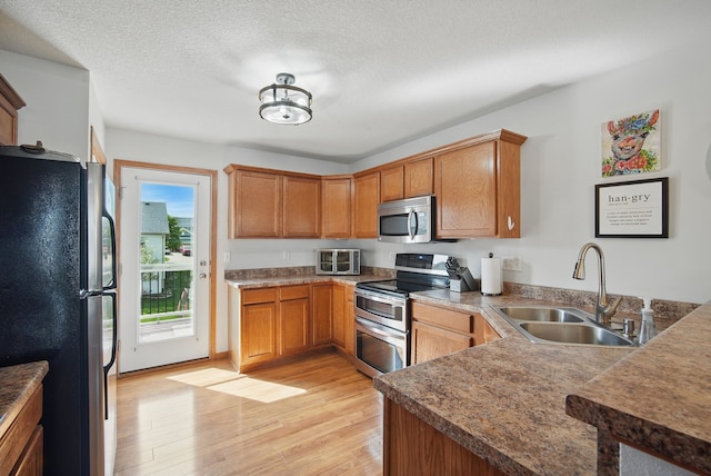 kitchen featuring brown cabinets, appliances with stainless steel finishes, a sink, and light wood finished floors