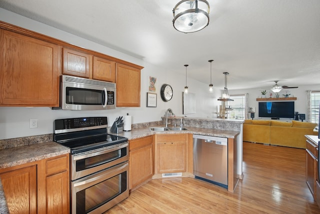 kitchen with appliances with stainless steel finishes, a sink, a peninsula, open floor plan, and a ceiling fan