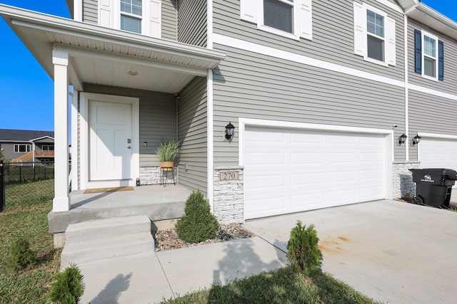 entrance to property featuring fence, driveway, stone siding, and a garage