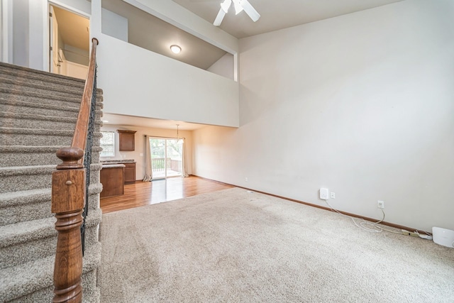 unfurnished living room featuring lofted ceiling with beams, light carpet, stairs, a ceiling fan, and baseboards