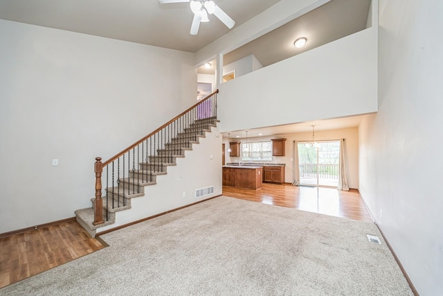 unfurnished living room with light colored carpet, ceiling fan with notable chandelier, stairs, baseboards, and visible vents