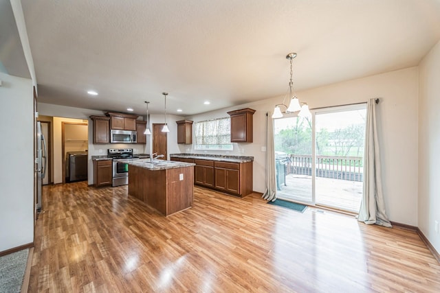 kitchen with a kitchen island with sink, wood finished floors, a sink, hanging light fixtures, and stainless steel appliances
