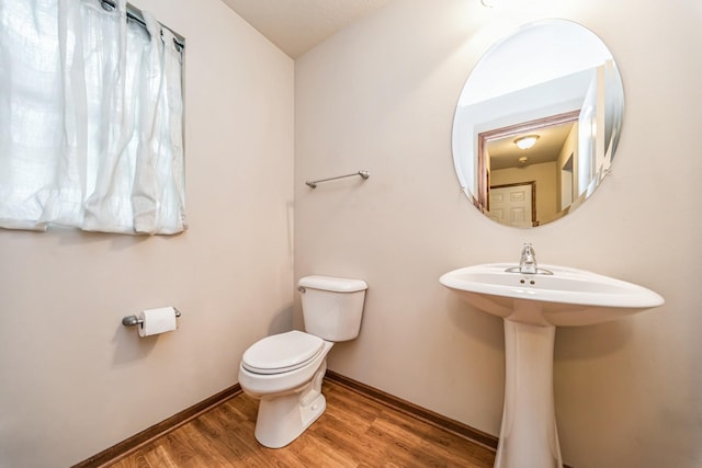 half bath with baseboards, toilet, and wood finished floors