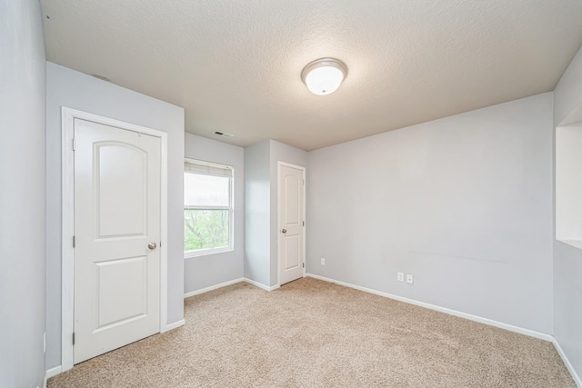 unfurnished bedroom featuring a textured ceiling, baseboards, light colored carpet, and visible vents