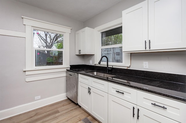 kitchen with light wood-type flooring, dishwasher, a sink, baseboards, and dark stone countertops