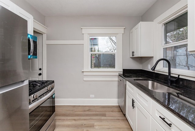 kitchen with a sink, light wood-style floors, dark stone countertops, stainless steel appliances, and baseboards