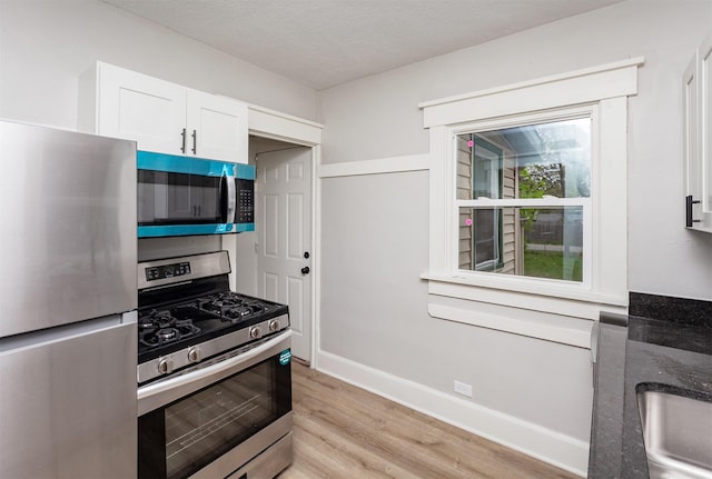kitchen with appliances with stainless steel finishes, dark stone counters, white cabinetry, baseboards, and light wood-type flooring