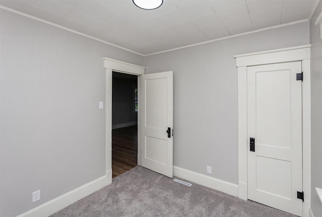 unfurnished bedroom with crown molding, carpet floors, baseboards, and visible vents