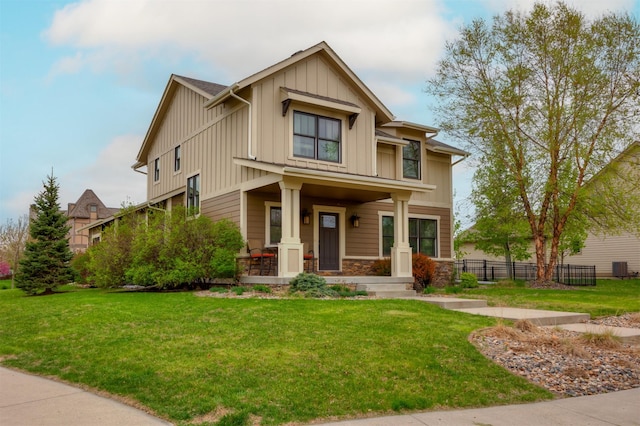 craftsman-style home featuring fence, covered porch, stone siding, a front yard, and board and batten siding