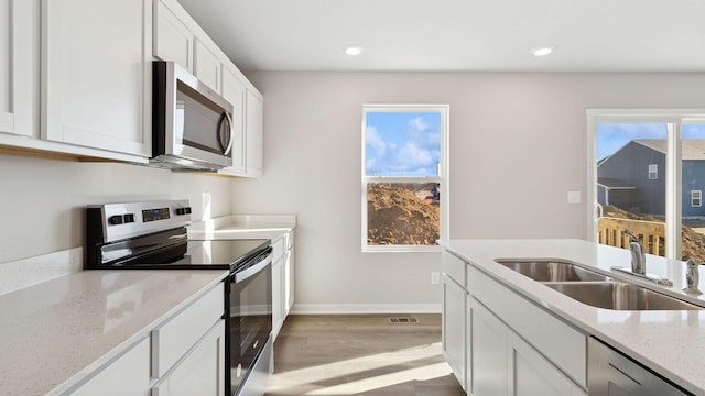 kitchen featuring baseboards, white cabinetry, a sink, light wood-style flooring, and stainless steel appliances