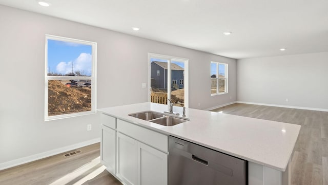 kitchen with stainless steel dishwasher, visible vents, a kitchen island with sink, a sink, and light wood-style flooring