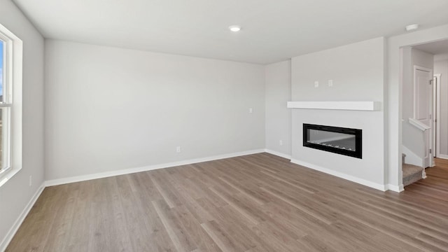 unfurnished living room with a glass covered fireplace, baseboards, stairway, and wood finished floors