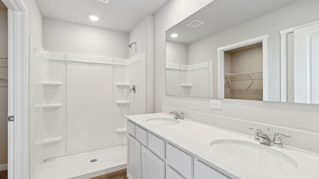 bathroom featuring double vanity, a sink, a walk in closet, and a stall shower
