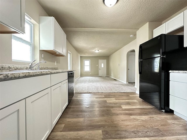 kitchen featuring a textured ceiling, arched walkways, white cabinets, freestanding refrigerator, and dishwashing machine