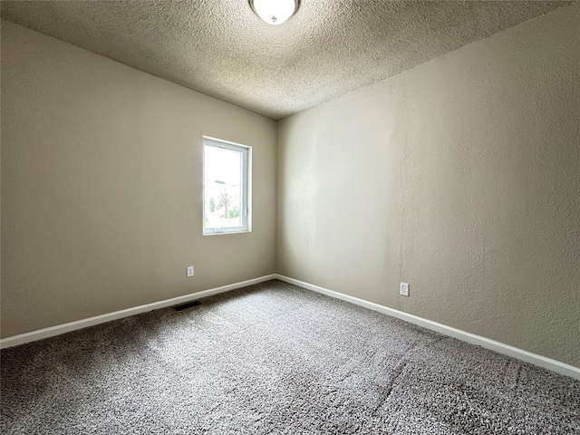empty room with carpet flooring, a textured ceiling, visible vents, and baseboards